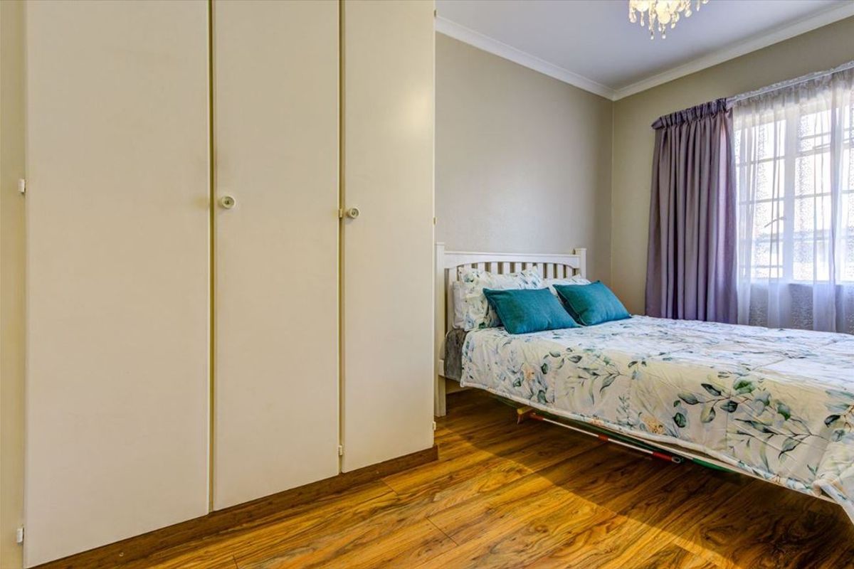 A well-maintained bedroom featuring laminate flooring, neutral wall tones, and ample built-in cupboard storage space.