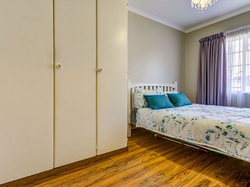 A well-maintained bedroom featuring laminate flooring, neutral wall tones, and ample built-in cupboard storage space.