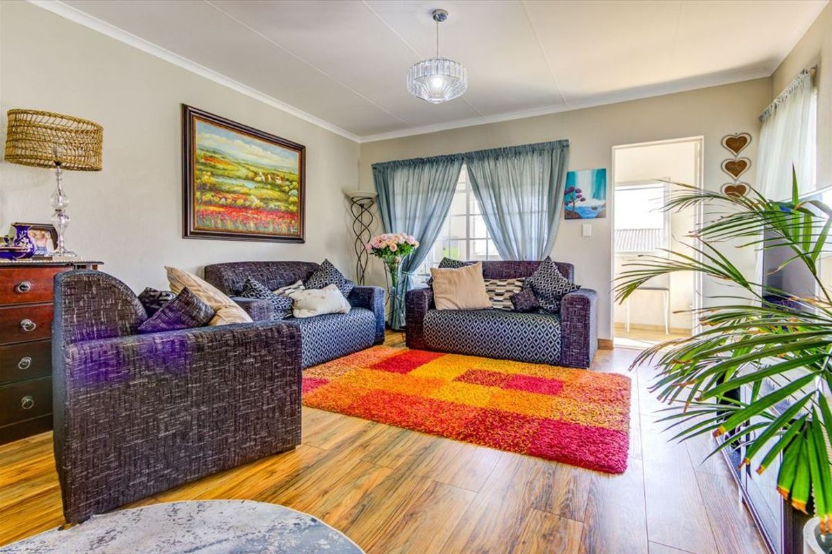 A comfortable living room featuring laminate flooring, neutral wall tones, and a central pendant light fixture, with direct access to an adjoining outdoor space.