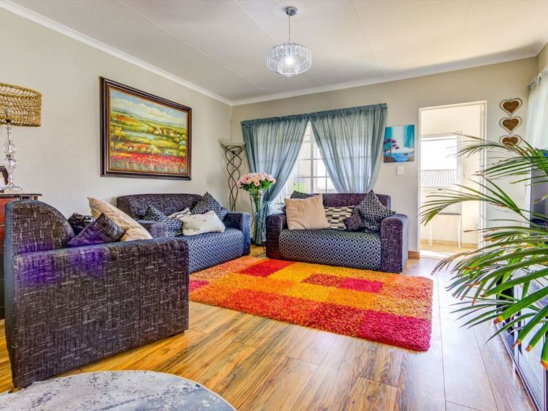 A comfortable living room featuring laminate flooring, neutral wall tones, and a central pendant light fixture, with direct access to an adjoining outdoor space.
