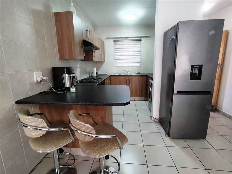 A functional kitchen featuring wood-finish cabinetry, dark laminate countertops, a breakfast bar, and tiled flooring with a neutral backsplash.