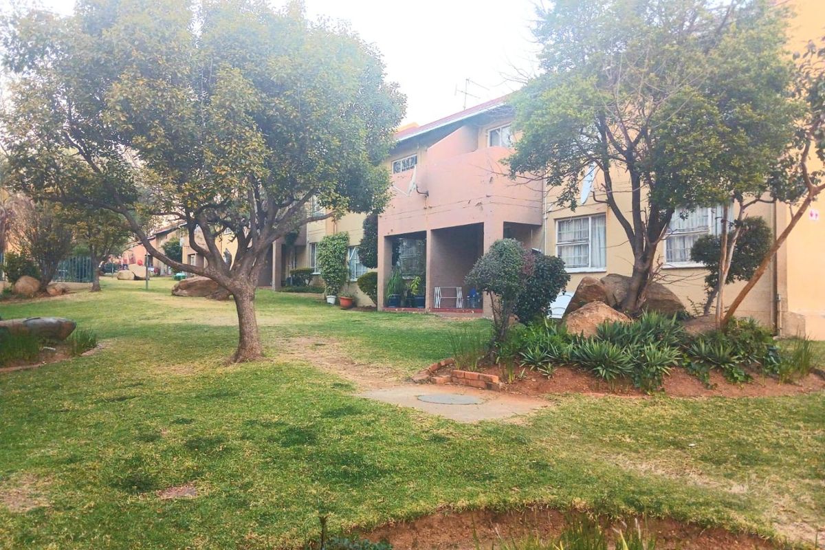 A view of the apartment complex rear elevation featuring a shared landscaped garden area and covered patio access.