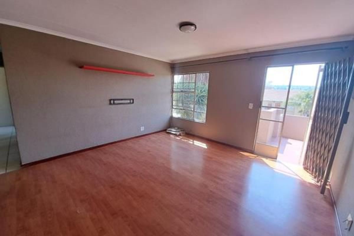 An empty living room featuring laminate flooring, a wall-mounted shelf, and a sliding door leading to an outdoor area with a security gate.