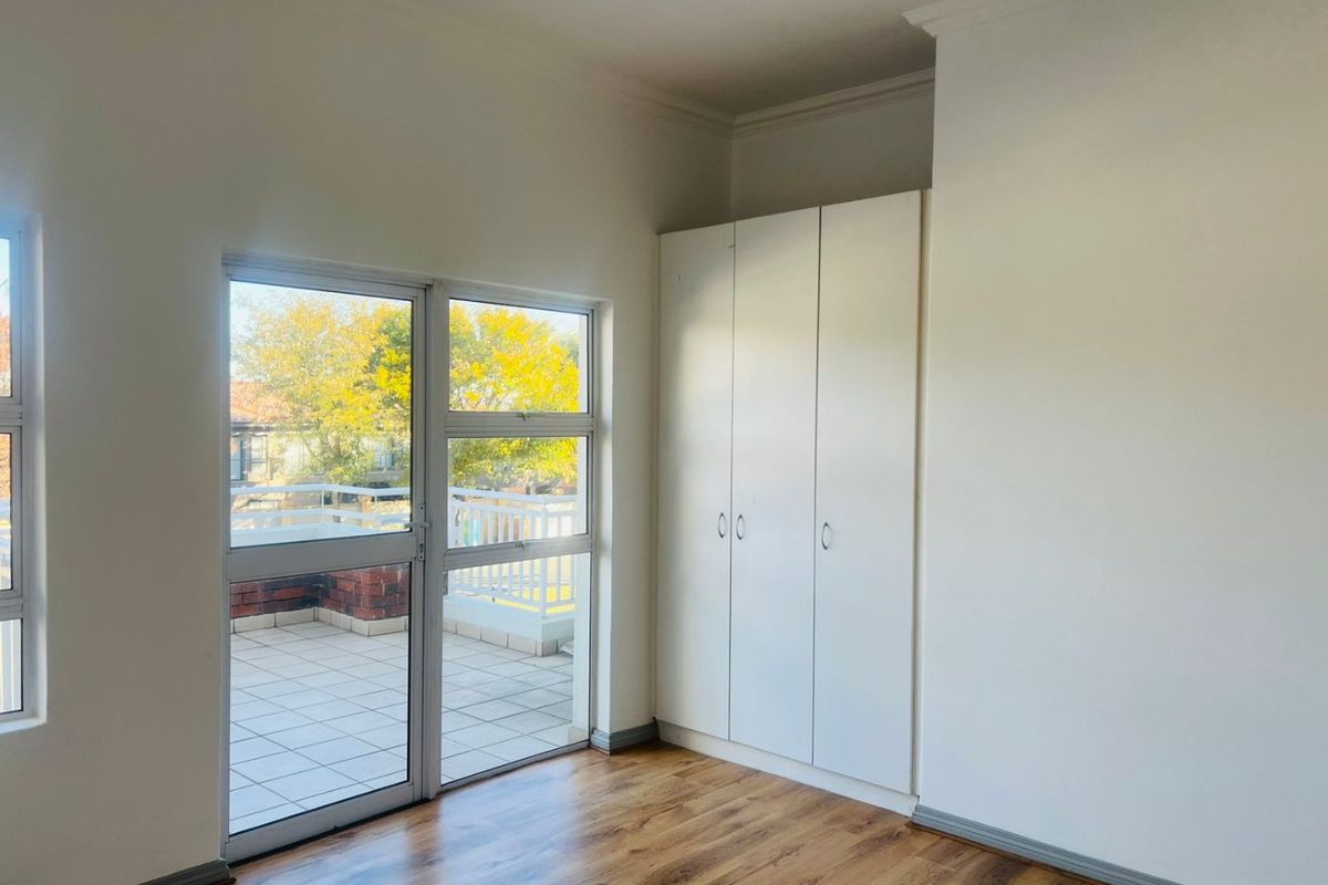 A bright, empty bedroom featuring laminate flooring, built-in cupboards, and a sliding door providing access to an outdoor balcony area.