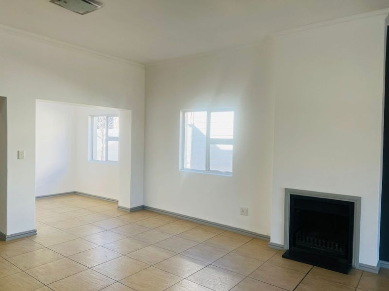 A bright, empty living room featuring neutral tiled flooring, a built-in fireplace, and clean white walls, offering a versatile space for customization.