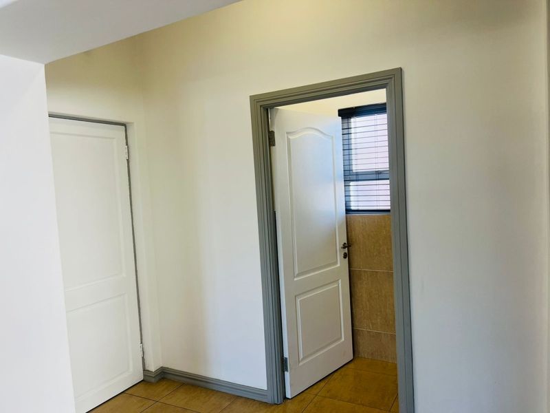A clean, neutral hallway featuring tiled flooring, white walls, and contrasting grey door frames leading to adjacent rooms.