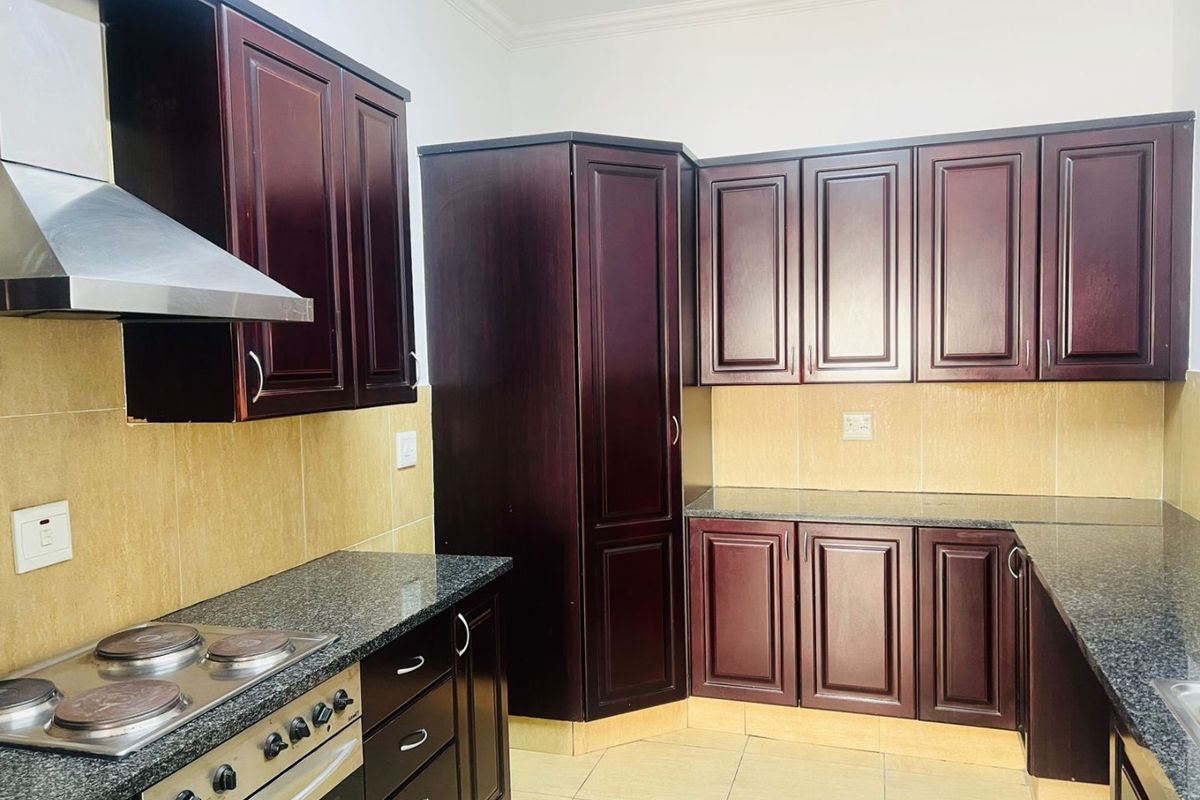 A functional kitchen featuring dark wood cabinetry, granite countertops, a built-in electric stove, and a stainless steel extractor fan with tiled finishes.