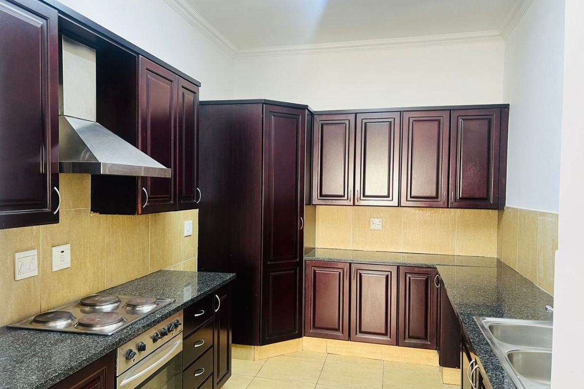 A well-maintained kitchen featuring dark wood cabinetry, granite countertops, built-in oven, electric hob, and a stainless steel extractor fan.