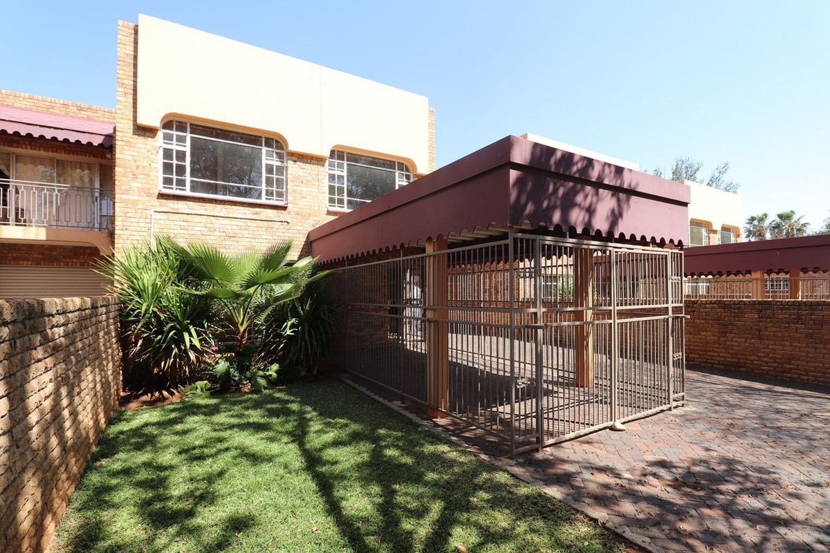 Rear exterior view of the townhouse featuring a brick facade, a paved driveway area, and a covered metal carport structure.