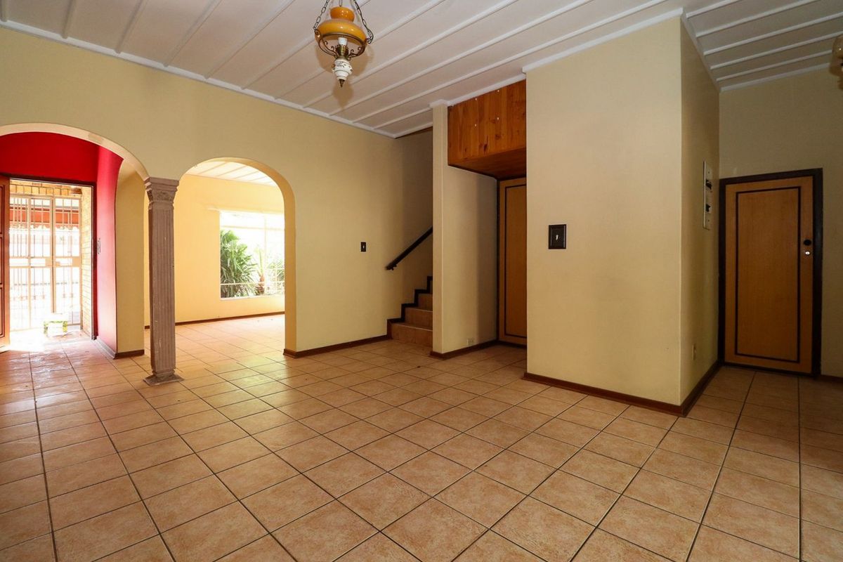 Spacious, empty living area featuring tiled flooring, architectural archways, a decorative column, and a staircase leading to the upper level.