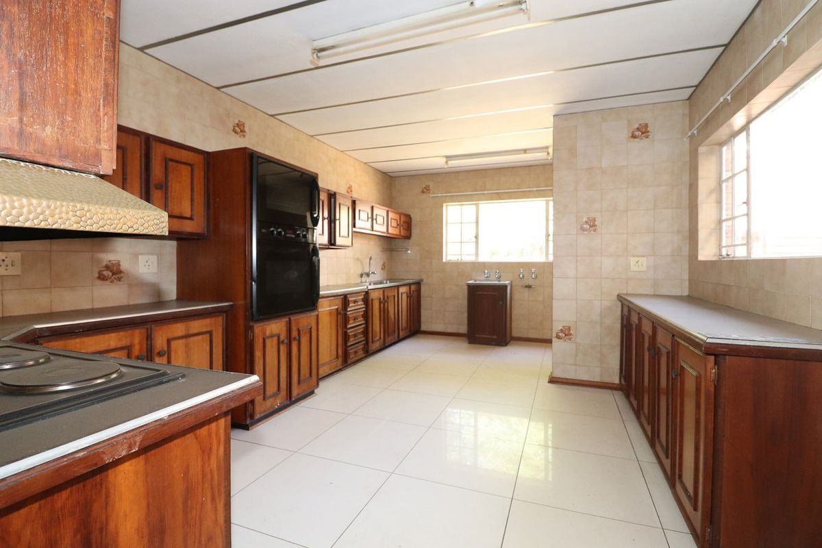 Spacious kitchen featuring extensive wooden cabinetry, built-in oven, hob, and tiled finishes, offering a functional layout ready for modern updates.