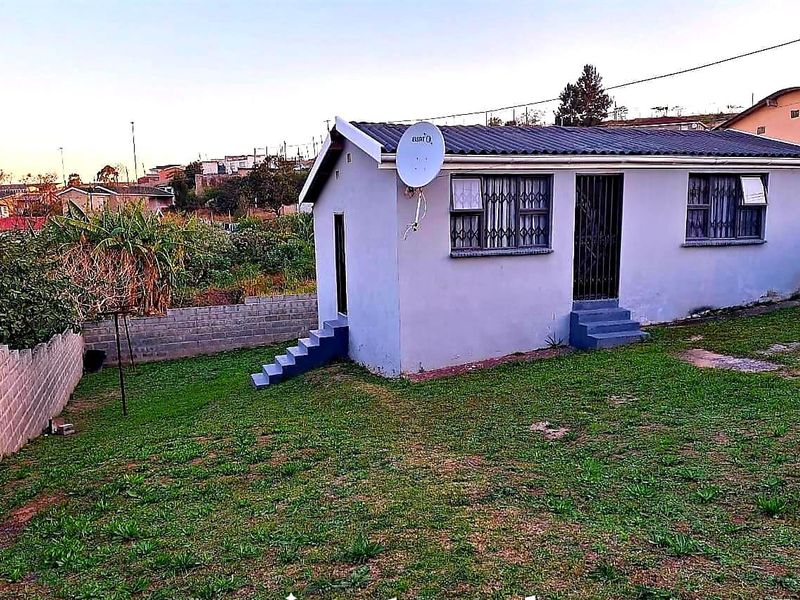 Rear view of a detached house featuring a tiled roof, security bars on windows, and a concrete block boundary wall in a residential setting.