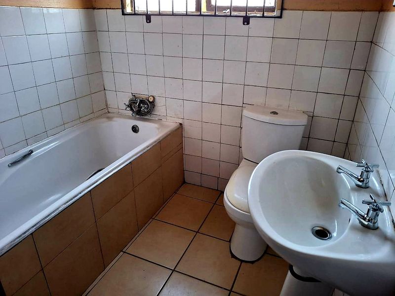 A functional bathroom featuring a bathtub, pedestal basin, and toilet with tiled finishes, offering potential for modernization and cosmetic updates.