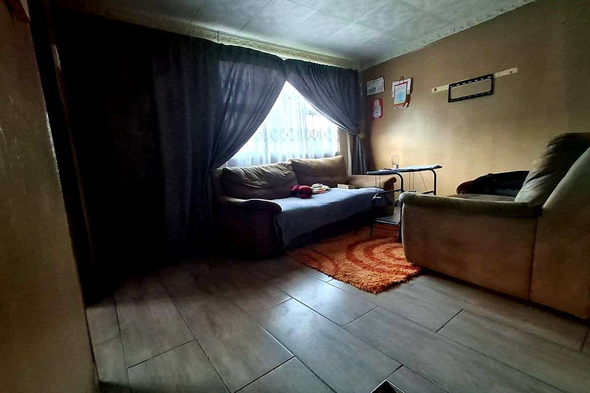 A living room featuring tiled flooring and ceiling tiles, currently requiring cosmetic updates to the wall finishes and ceiling.