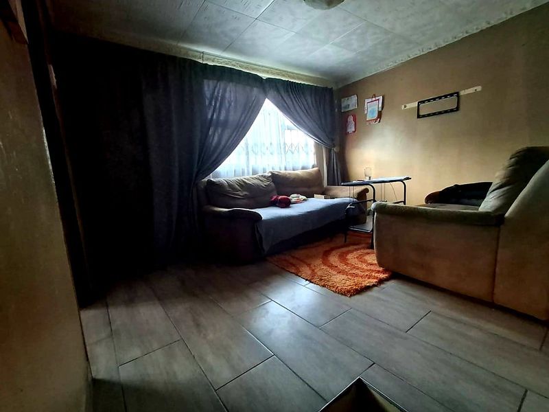 A living room featuring tiled flooring and ceiling tiles, currently requiring cosmetic updates to the wall finishes and ceiling.