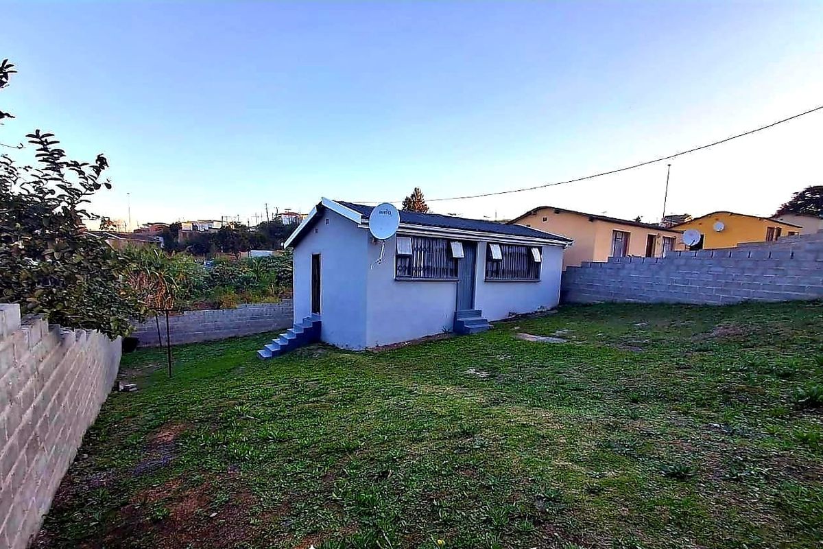 Rear view of a detached house featuring a concrete block boundary wall, metal security bars on windows, and a small lawn area.