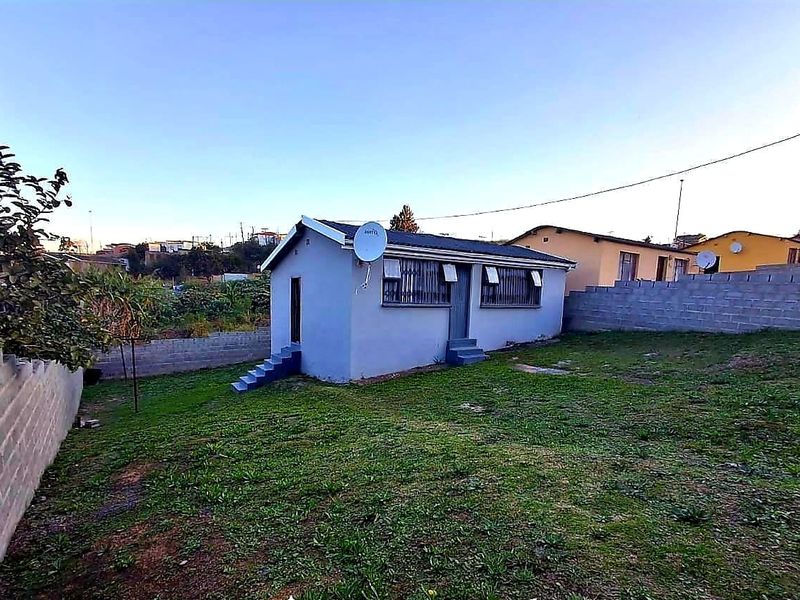 Rear view of a detached house featuring a concrete block boundary wall, metal security bars on windows, and a small lawn area.