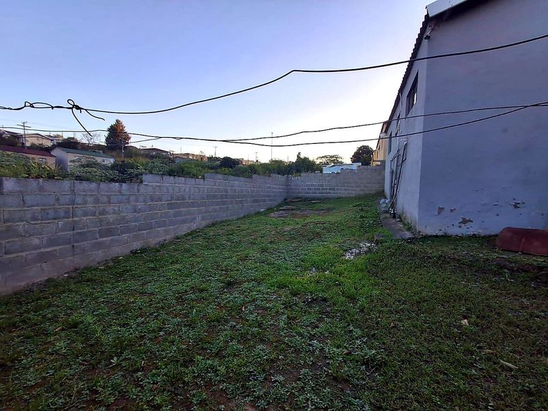 A rear yard area featuring a concrete block boundary wall and an exterior wall with visible paint deterioration.