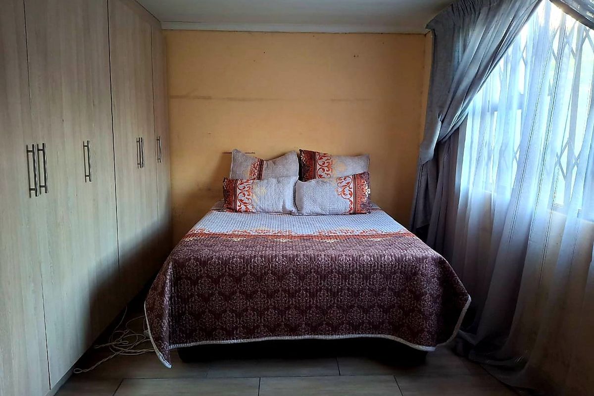 A bedroom featuring built-in cupboards, tiled flooring, and a window with a security gate.