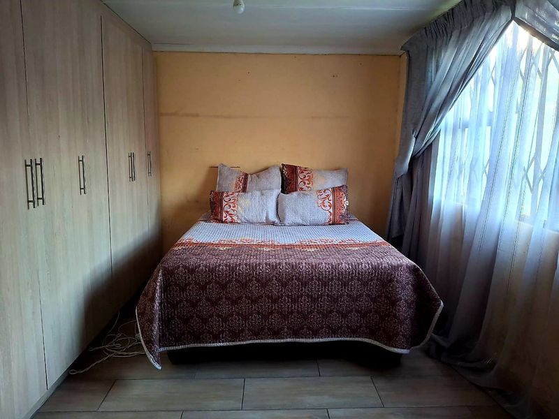 A bedroom featuring built-in cupboards, tiled flooring, and a window with a security gate.
