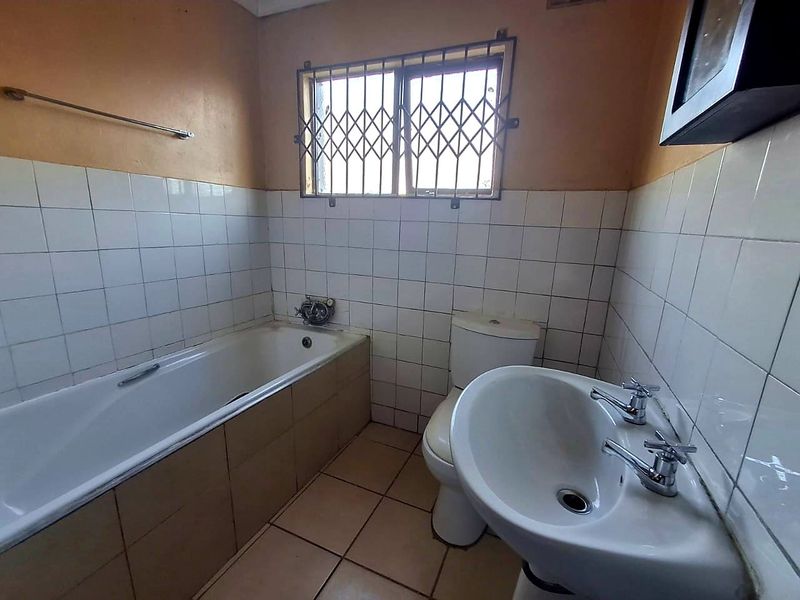 A functional bathroom featuring a bathtub, pedestal basin, and toilet, finished with tiled walls and flooring, requiring cosmetic updates.