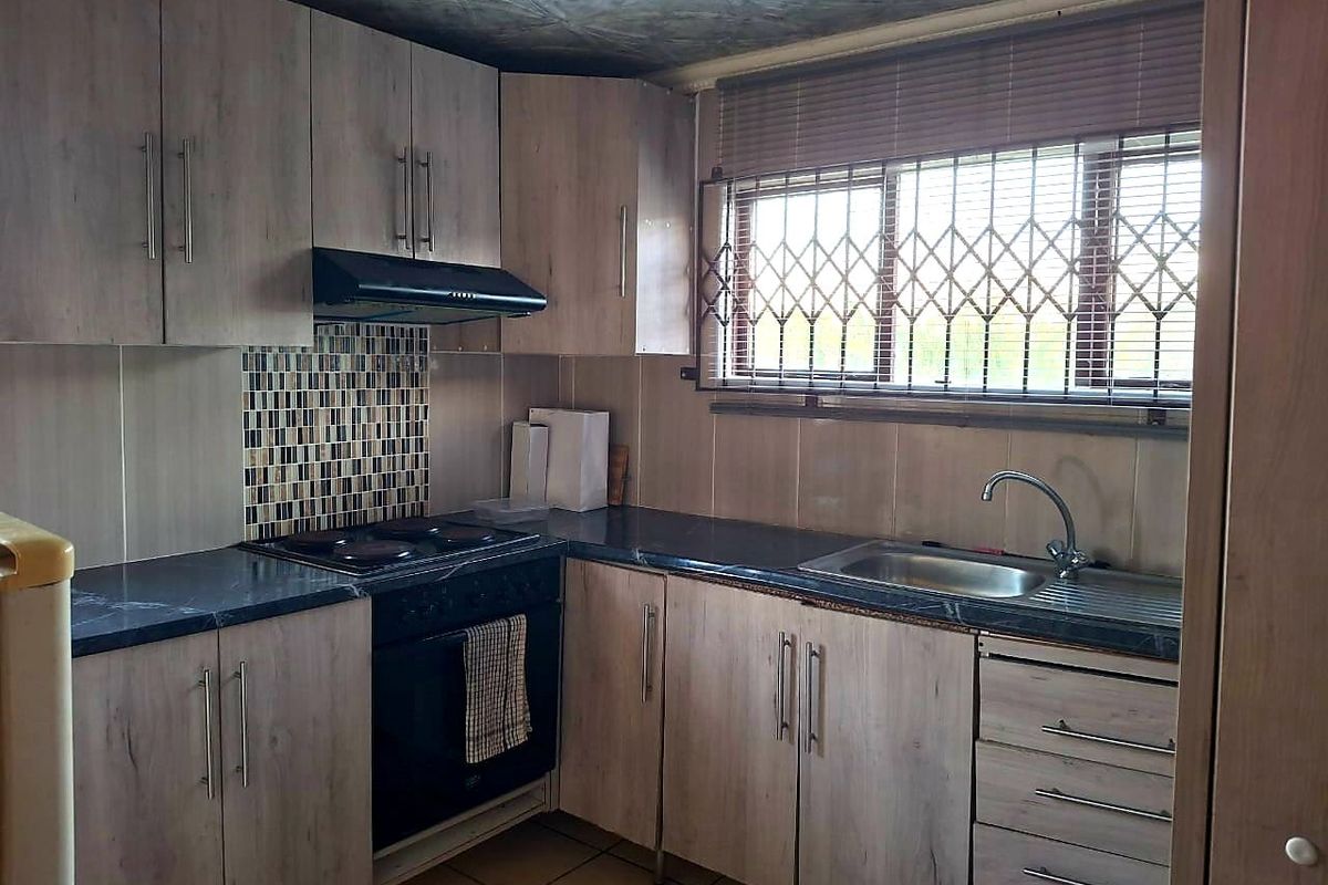 Functional kitchen featuring wood-look cabinetry, dark laminate countertops, built-in oven with hob, and a stainless steel sink with window security gate.