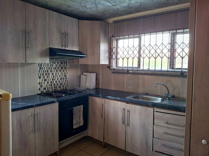 Functional kitchen featuring wood-look cabinetry, dark laminate countertops, built-in oven with hob, and a stainless steel sink with window security gate.