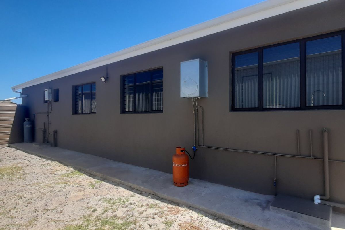 Rear exterior view of the property featuring a water tank, gas geyser installation, and concrete pathway along the building wall.