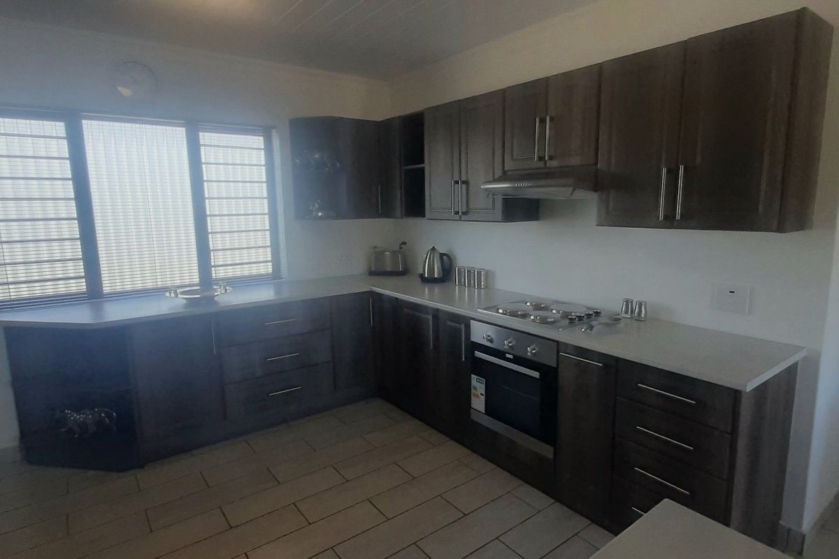A functional kitchen featuring dark wood cabinetry, stone countertops, a built-in oven, gas hob, and tiled flooring.