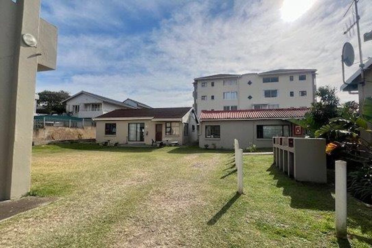 A view of the rear exterior area featuring a shared lawn, built-in braai facilities, and access to the townhouse units.