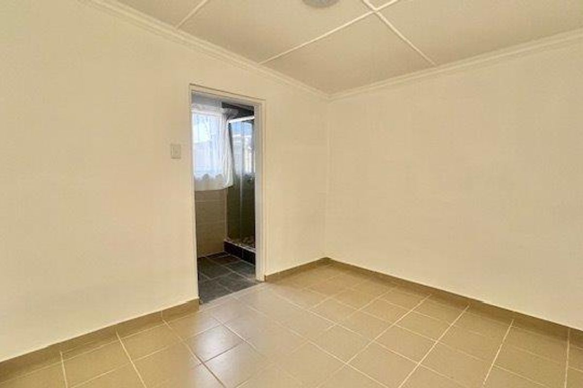 A clean, empty bedroom featuring neutral tiled flooring and a coved ceiling, with direct access to an adjoining en-suite bathroom.