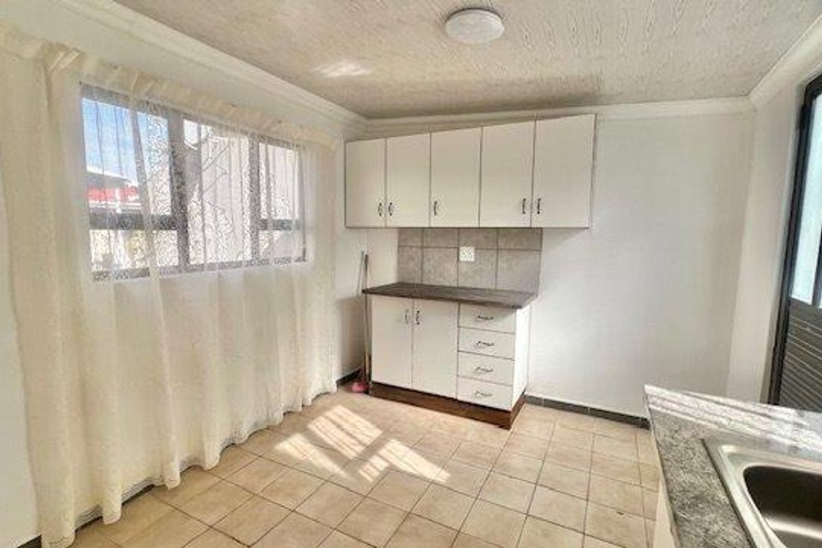 A functional kitchen area featuring built-in white cabinetry, tiled splashbacks, and a stainless steel sink, offering a clean and practical layout.