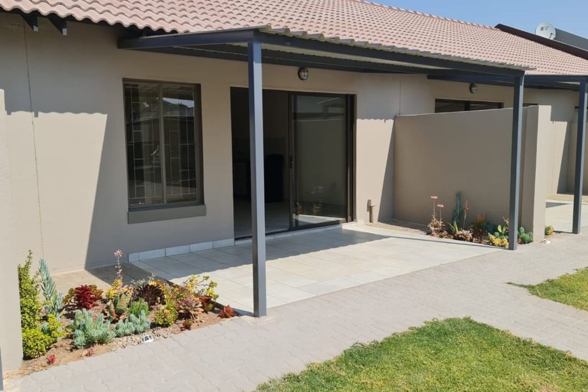 Rear view of the townhouse featuring a covered tiled patio, sliding glass doors, and a well-maintained garden area with paved pathways.