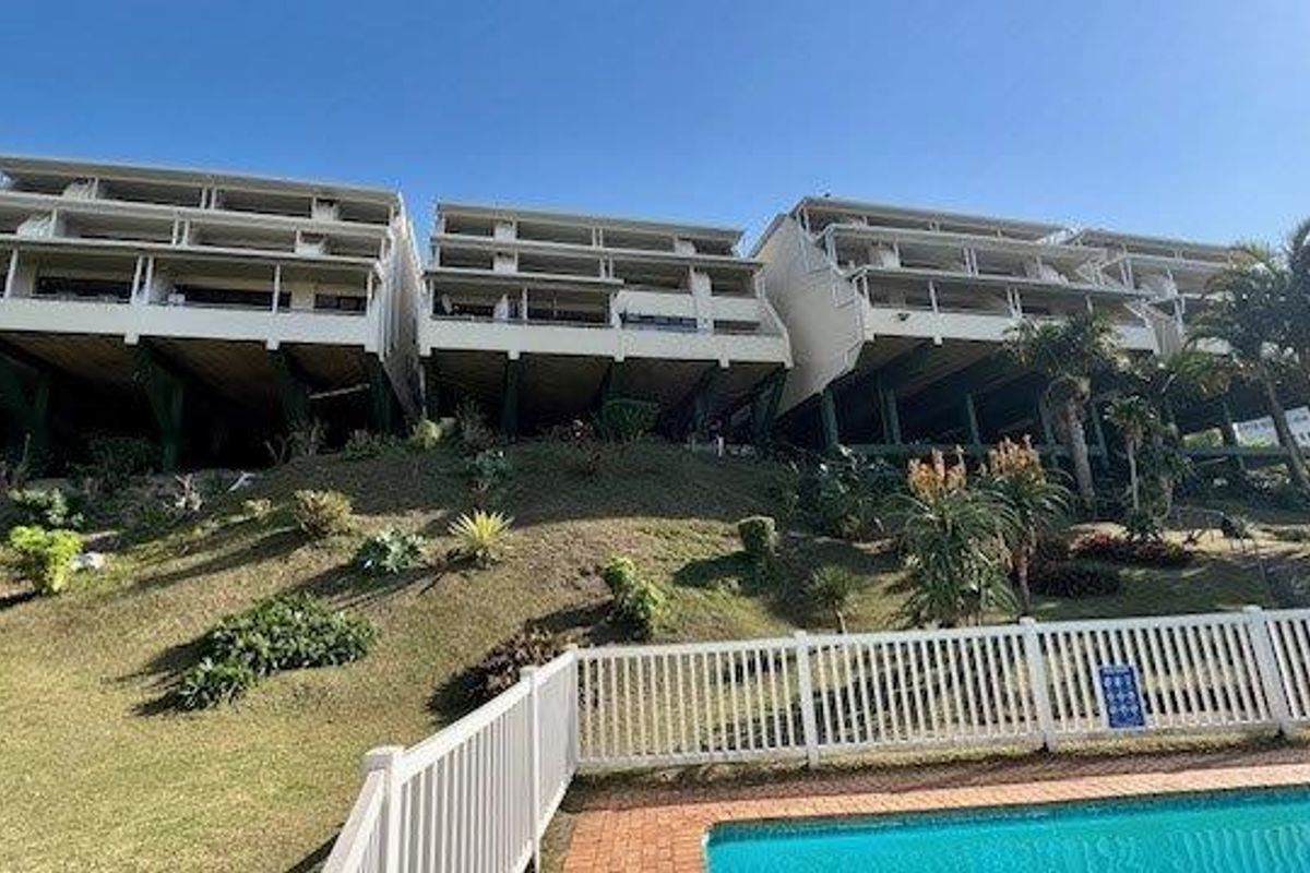 Rear view of a multi-story apartment complex featuring elevated balconies, stilt foundations, and a swimming pool area with a landscaped garden.