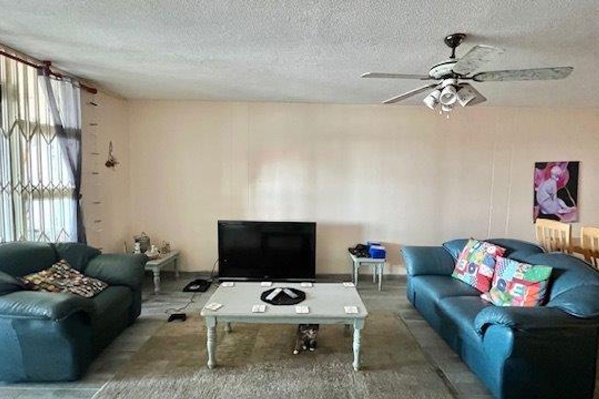 Spacious living room featuring a ceiling fan, tiled flooring, and a security gate leading to the outdoor area.