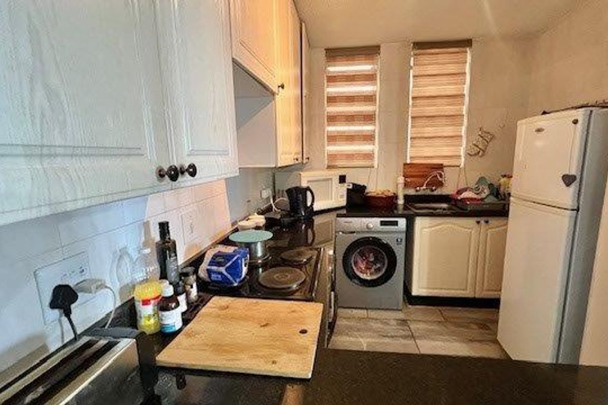 Compact kitchen featuring white cabinetry, dark countertops, integrated washing machine, and dual windows with roller blinds.