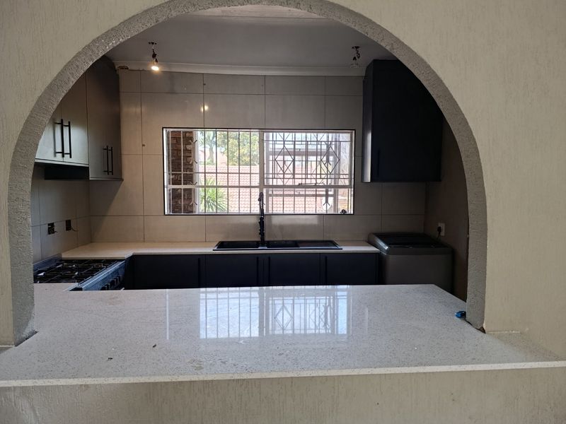 Modernized kitchen featuring dark cabinetry, stone countertops, gas hob, and a breakfast bar, framed by a decorative architectural archway.