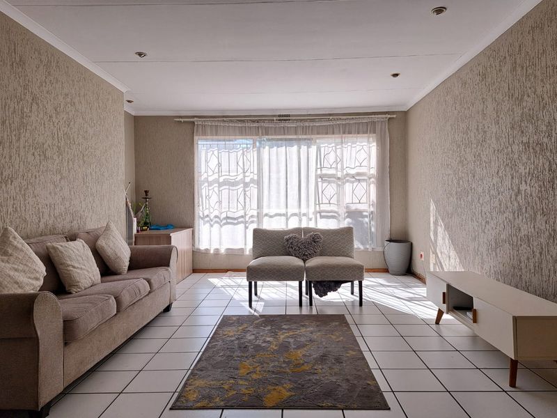 A bright living room featuring tiled flooring, recessed ceiling lighting, and a large window with security bars, offering a neutral canvas for personalization.
