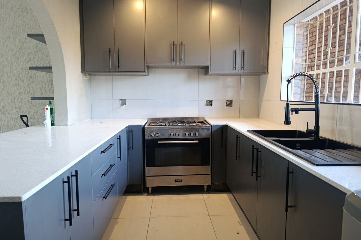 Modern kitchen featuring dark grey cabinetry, white quartz countertops, a gas stove with oven, and a contemporary black double sink with gooseneck faucet.