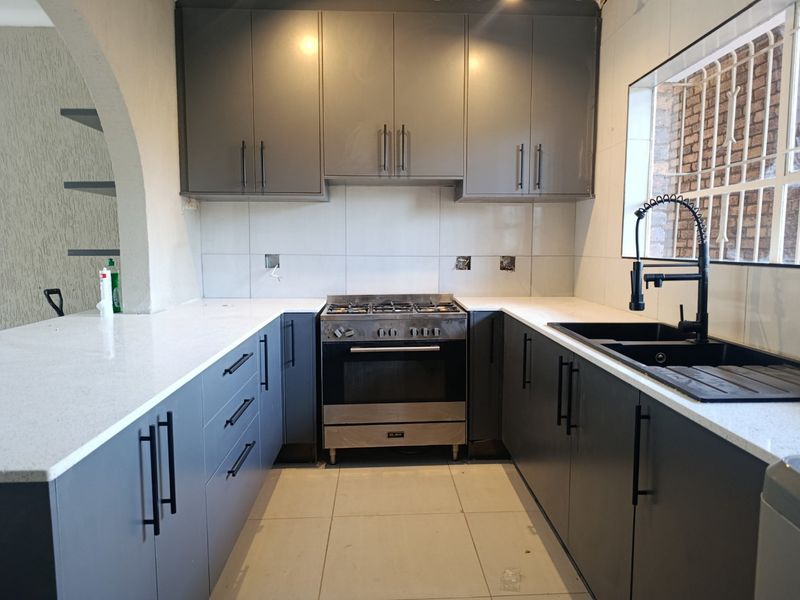 Modern kitchen featuring dark grey cabinetry, white quartz countertops, a gas stove with oven, and a contemporary black double sink with gooseneck faucet.
