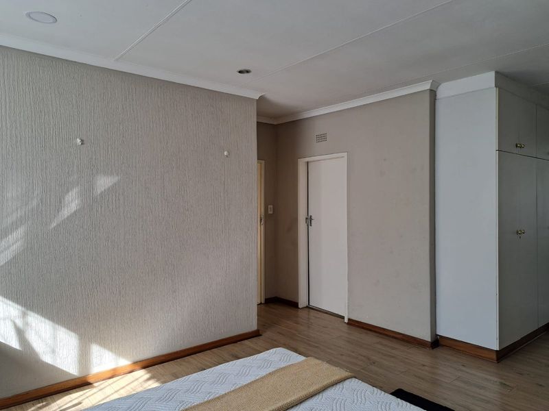 A spacious bedroom featuring laminate flooring, built-in cupboards, and neutral wall finishes, offering a blank canvas for personalization.