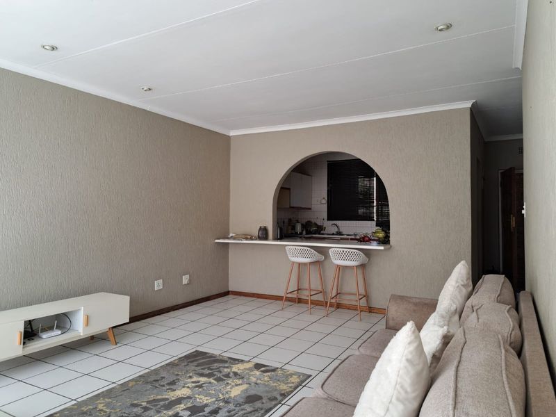 Open plan living area featuring tiled flooring, recessed lighting, and a distinctive arched serving hatch connecting to the kitchen.