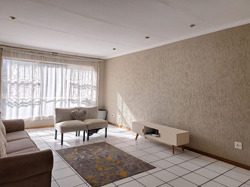 A bright living room featuring tiled flooring, textured feature wall, and recessed downlights, offering a neutral canvas for interior design updates.