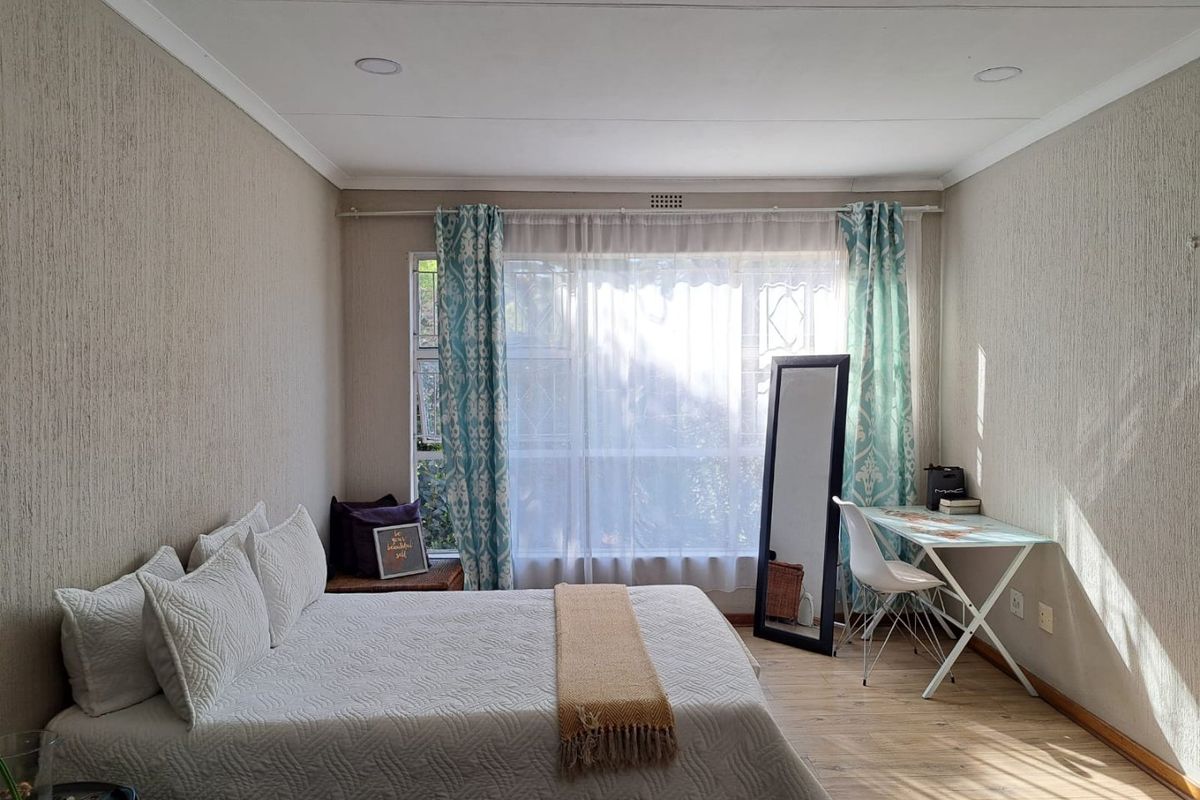 A well-lit bedroom featuring textured wallpaper, laminate flooring, and recessed ceiling lighting, with a large window fitted with security bars.