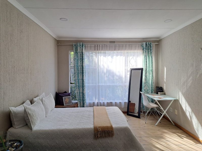 A well-lit bedroom featuring textured wallpaper, laminate flooring, and recessed ceiling lighting, with a large window fitted with security bars.