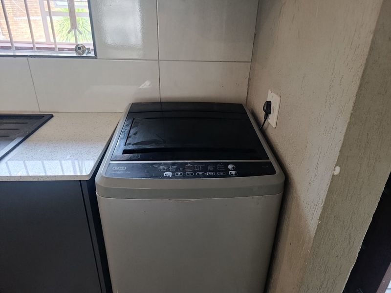A functional laundry area featuring a stone countertop, tiled splashback, and dedicated space for a washing machine.