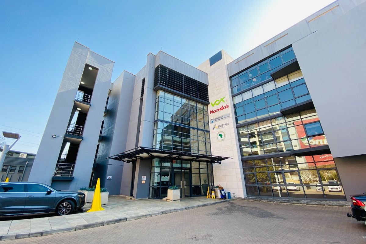 Modern commercial office building facade featuring extensive glass curtain walling, a prominent entrance canopy, and a dedicated stairwell tower.