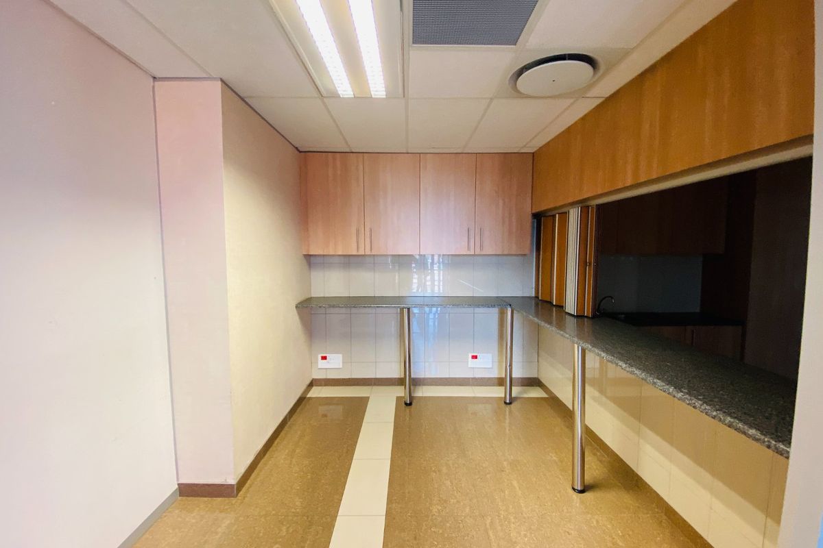 A clean, empty commercial kitchen area featuring built-in cabinetry, granite countertops, tiled backsplash, and integrated ceiling lighting.
