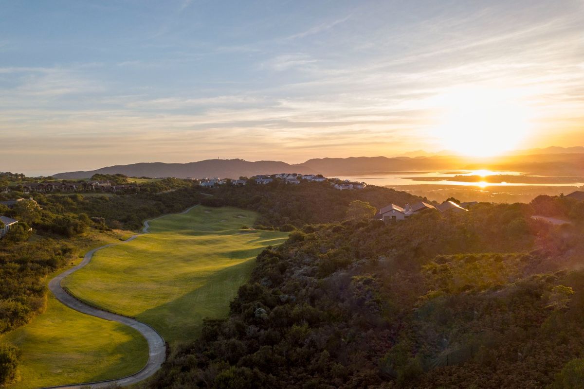 An aerial view of a golf course landscape at sunset, showcasing the rolling green fairways and surrounding natural terrain.