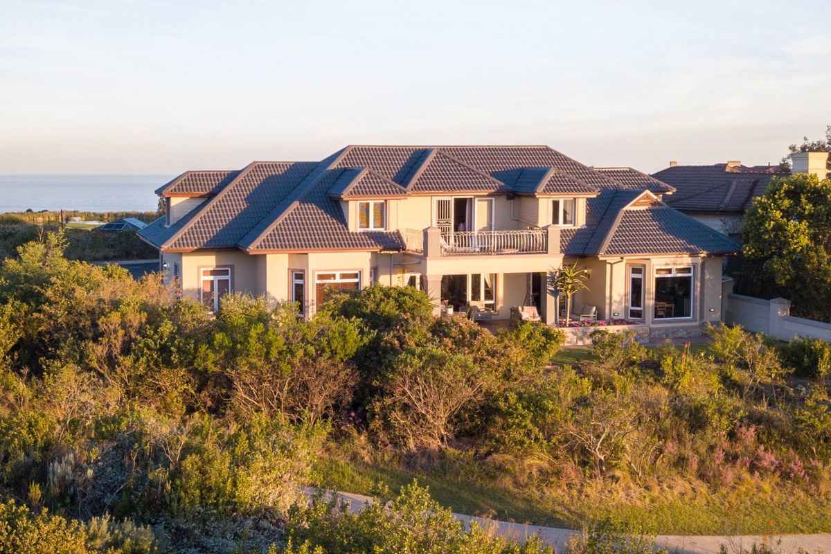 An elevated view of the rear elevation of a large residential property featuring a tiled roof, balcony, and extensive landscaped garden surroundings.